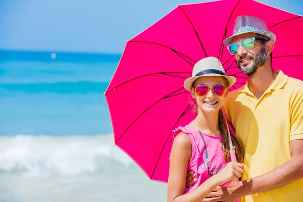 Menina e pai com um guarda-chuva rosa na praia de areia — Fotografia de Stock