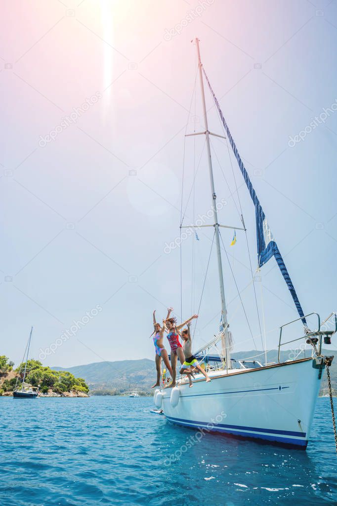 Happy family jump in sea of sailing yacht on summer cruise. Travel adventure, yachting with child on family vacation.