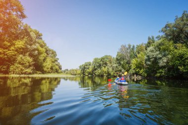 Mutlu çocuklar yaz tatilinde güneşli bir günde nehirde kano yapıyorlar.