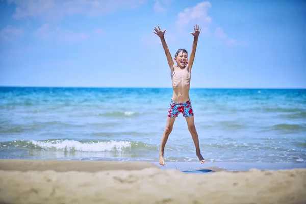 Entzückender glücklicher Junge springt und spielt am Strand. — Stockfoto