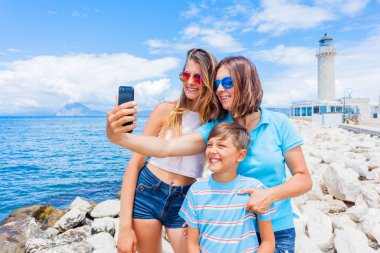 Happy family making selfie in front of Patras lighthouse, Peloponnese, Greece. clipart