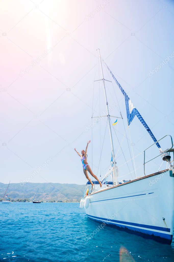 Girl jump in sea of sailing yacht on summer cruise. Travel adventure, yachting with child on vacation.