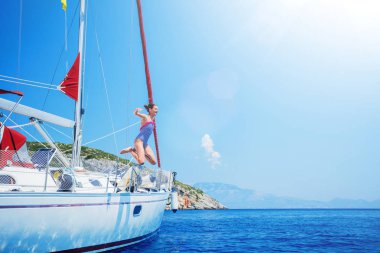 Girl jump in sea of sailing yacht on summer cruise. Travel adventure, yachting with child on vacation. clipart
