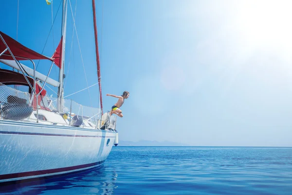 Rapaz saltar no mar de iate à vela em cruzeiro de verão. Viagem aventura, iatismo com criança em férias . — Fotografia de Stock