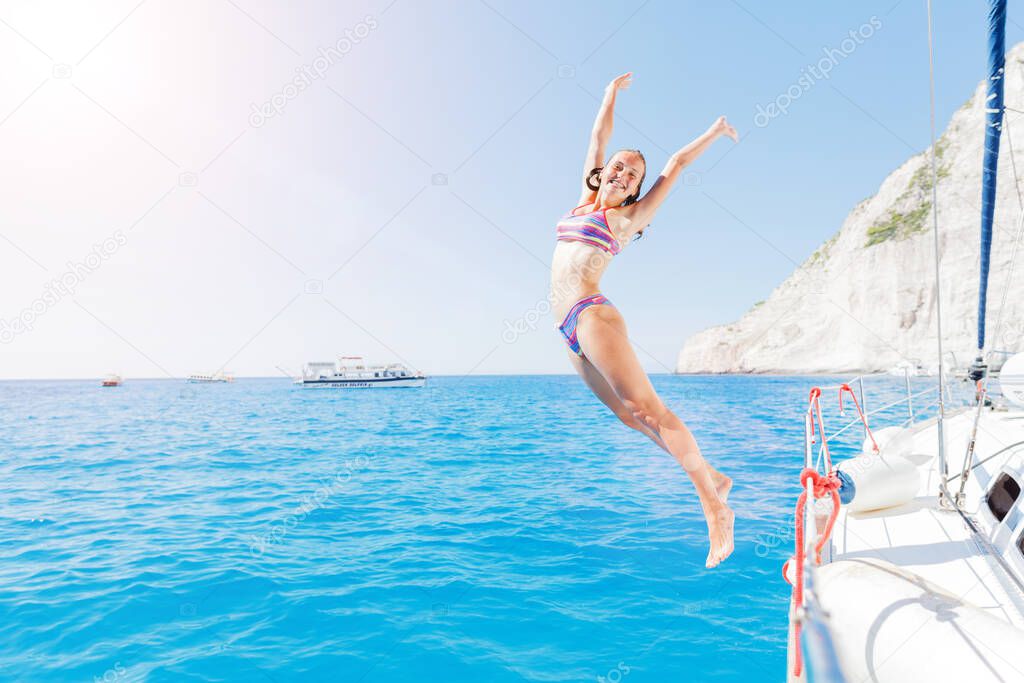 Girl jump in sea of sailing yacht on summer cruise. Travel adventure, yachting with child on vacation.