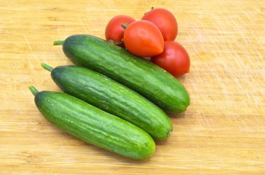 Tahtada taze ve sağlıklı yeşil salatalık ve domates var.