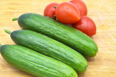 Tahtada taze ve sağlıklı yeşil salatalık ve domates var.