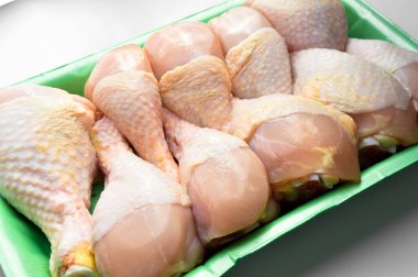 Taze pişmemiş tavuk budu parçaları, yeşil pakette pişmeye hazır bebek, beyaz arka planda.