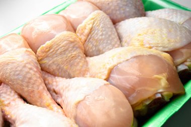 Taze pişmemiş tavuk budu parçaları, yeşil pakette pişmeye hazır bebek, beyaz arka planda.
