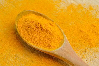 Bambu ahşap arka planda ahşap kaşıkta taze zerdeçal tozu.