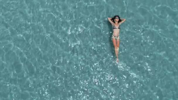 Belle jeune femme flottant dans l'eau cristalline, plan aérien rotatif 