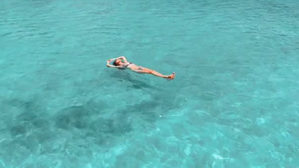 Schöne junge Frau, die im kristallklaren Wasser schwimmt, Drehschuss aus der Luft — Stockvideo