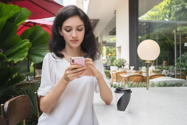 Menina bonita assistindo suas fotos no smartphone enquanto relaxa no café — Fotografia de Stock