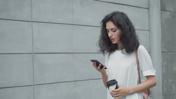 Jonge vrouw met smartphone wandelen in de stad, steadicam schot — Stockvideo