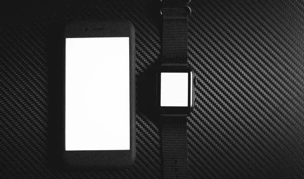 Черный смартфон и черные часы на столе из углеродного волокна — стоковое фото