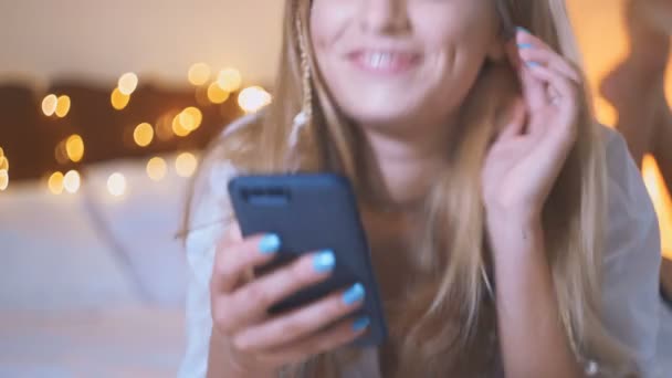 Menina loira bonita usar seu telefone celular enquanto deitado na cama. namoro na internet, close-up — Vídeo de Stock