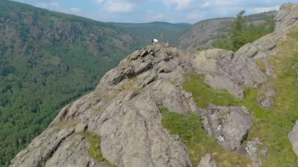 En ung kvinna sitter på kanten av en klippa med imponerande berg — Stockvideo