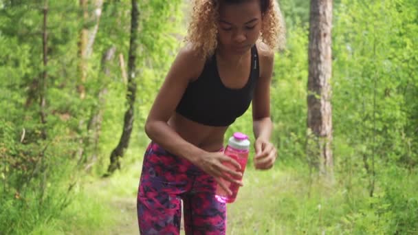 Schwarze Frau trinkt aus rosa Flasche. Porträt einer schwarzen jungen Frau beim Joggen — Stockvideo