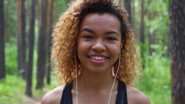 young beautiful black girl with curly hair walking after jogging, smiling and looking at the camera