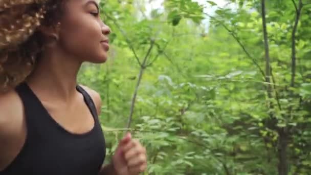 Молодая красивая афроамериканка с вьющимися волосами, бегущая в сосновом лесу, крупным планом — стоковое видео