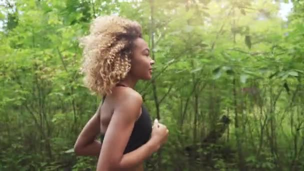 Νέοι όμορφη αφρικανική αμερικανική γυναίκα με σγουρά μαλλιά που τρέχει σε ένα δάσος, κοντινό πλάνο — Αρχείο Βίντεο