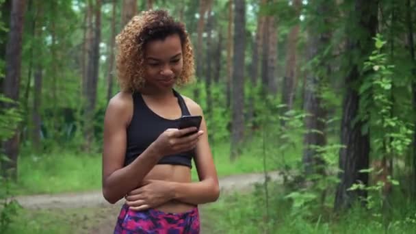 Jeune belle femme afro-américaine aux cheveux bouclés bavarde dans son téléphone avant de faire du jogging — Video