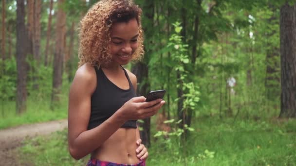 Jeune belle femme afro-américaine aux cheveux bouclés bavarde dans son téléphone avant de faire du jogging — Video