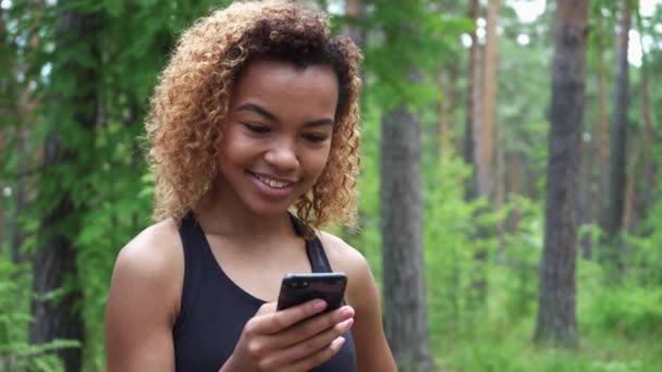 Svart ung kvinna använder sin smartphone efter jogging och visar grön skärm till kameran — Stockvideo