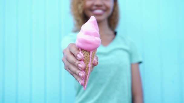 Feliz chica negra muestra rosa derretimiento helado y luego empezar a comer en fondo de la pared azul — Vídeos de Stock