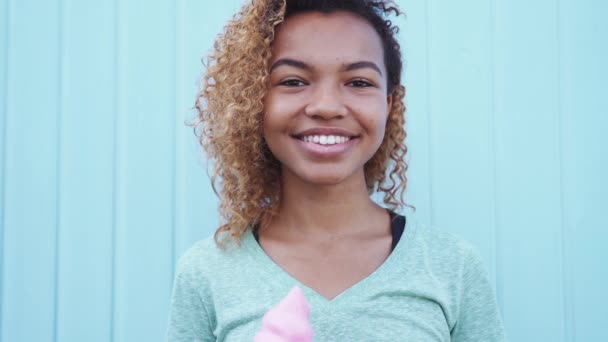 Happy černá dívka ukazuje růžové tání zmrzliny v pomalém pohybu na pozadí modré zdi — Stock video