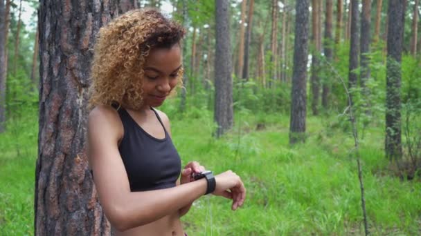 Mooie zwarte meisje met krullend haar draait op muziek en zet op hoofdtelefoons voor joggen — Stockvideo