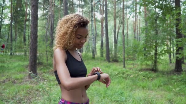 年轻美丽的非洲裔美国妇女与卷曲的头发使用她的智能手表慢跑 — 图库视频影像