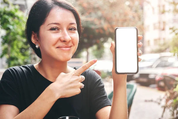 Щаслива красива жінка тримає і показує мобільний телефон з порожнім білим екраном в кафе — стокове фото