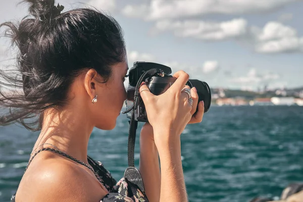 Black haired female travel photographer, taking pictures of landscape at sea