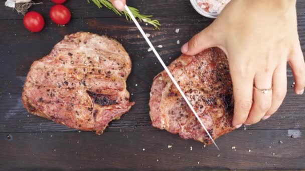 Frauenhände schneiden saftige Steaks vom Grill auf einem Holztisch — Stockvideo