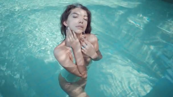 Молодая гламурная женщина в бикини стоит в бассейне на вилле и смотрит в камеру — стоковое видео