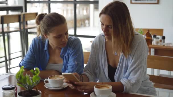 As mulheres têm um encontro no café. One Sharing algo emocionante em seu telefone móvel — Vídeo de Stock