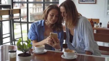 Two woman sharing coffee using smartphone in cafe