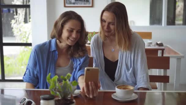 Dos mujeres compartiendo café con teléfono inteligente en la cafetería — Vídeo de stock