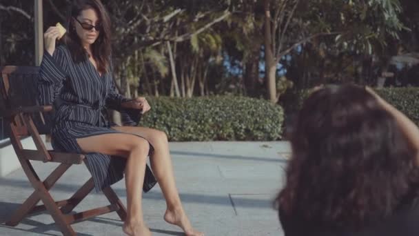 Жінка позує для жінки-фотографа на стільці біля басейну — стокове відео