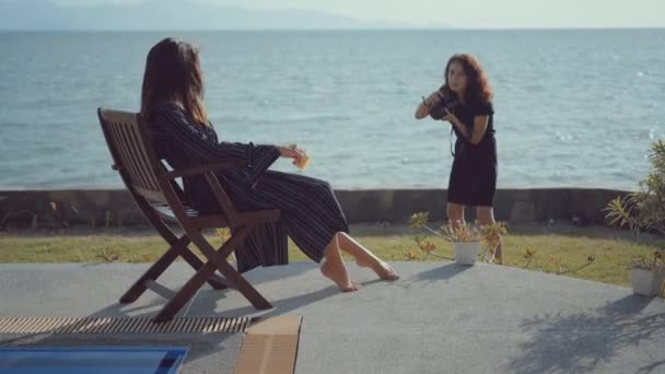 Vrouwelijke model vormt op een strandstoel voor vrouwelijke fotograaf — Stockvideo