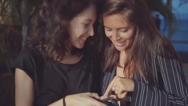 Twee vrouwen onderzoeken lachend foto's genomen op de camera — Stockvideo