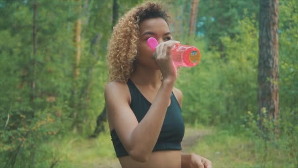 アクティブな黒人女性のピンク色のボトルから飲みます ジョギング ステディカム スローモーションで撮影しながら休憩を取って黒の若い女性の肖像画 — ストック動画