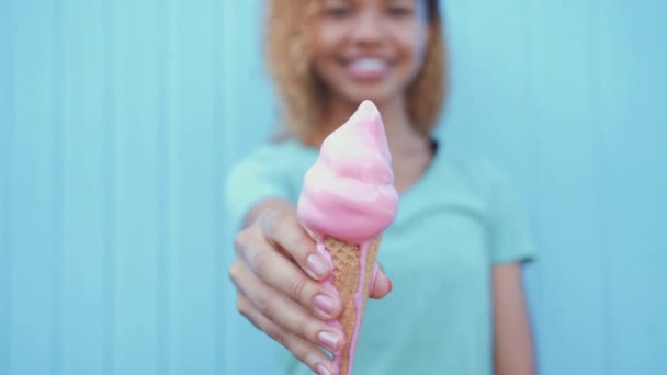 Young afro girl eating pink melting ice cream at blue wall background — Stock Video