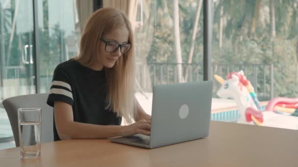 Mujer rubia se sienta en la mesa en casa en el ordenador portátil durante el día. concepto freelance — Vídeos de Stock