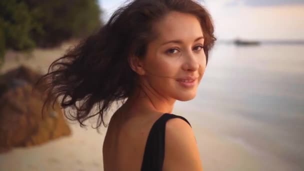 Çekici uzun saçlı kıvırcık esmer kadının arka görünümü kameraya döner ve güzel bir gülümseme verir — Stok video