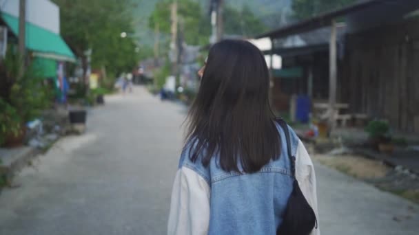 Arkadan görünüşü çekici uzun saçlı esmer kadın şehir cadde veya sokak yürüyüş, fotoğraf makinesinin için ve güzel bir gülümseme verir — Stok video
