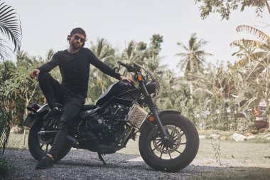 Siyah giyim yakışıklı bisikletçi adam klasik tarzı kafe yarışçı motosiklet oturup. özel yapım motosiklet