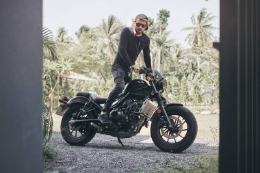 Siyah giyim yakışıklı bisikletçi adam klasik tarzı kafe yarışçı motosiklet oturup. özel yapım motosiklet