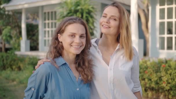 Happy lesbian couple standing on backyard of their house and look straight at camera — Stock Video